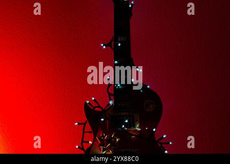 Elektrische Gitarre mit Weihnachtsdekoration an einer roten Wand Stockfoto