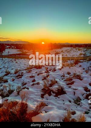 Ein atemberaubender Winteruntergang strahlt ein goldenes Leuchten über eine ruhige, schneebedeckte Landschaft und fängt die ruhige Schönheit der Natur in ihrer reinsten Form ein. Stockfoto