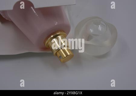 Gegenstände, Dinge, Kosmetik und Parfums. Eine schöne rosa Glasflasche mit Damenparfümen, goldenem Spray und weißer matter Plastikkappe mit einer weißen Box. Stockfoto