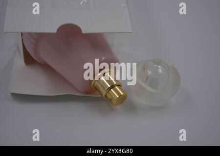 Gegenstände, Dinge, Kosmetik und Parfums. Eine schöne rosa Glasflasche mit Damenparfümen, goldenem Spray und weißer matter Plastikkappe mit einer weißen Box. Stockfoto