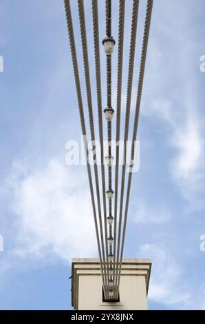 Die Aufhängungsseile und Lichter auf der Waco Hängebrücke erzeugen ein interessantes Muster vor einem blauen Himmel. Stockfoto