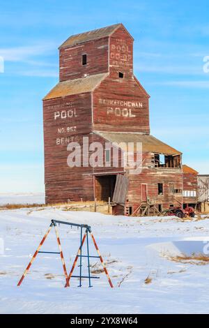 Ein großer brauner Kornelevator im Winter. Das Gebäude ist alt und hat eine Schaukel davor Stockfoto