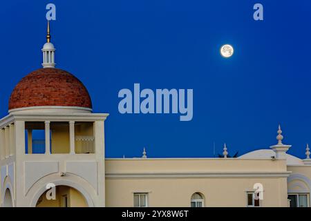 Ein großes weißes Gebäude mit einer roten Kuppel und einem großen Mond am Himmel. Das Gebäude ist von einem blauen Himmel umgeben Stockfoto