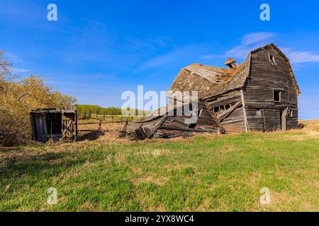 Ein baufälliges altes Bauernhaus befindet sich auf einem Feld mit blauem Himmel. Das Haus ist in einem Zustand des Verfallens, mit kaputten Fenstern und einem durchhängenden Dach. Th Stockfoto