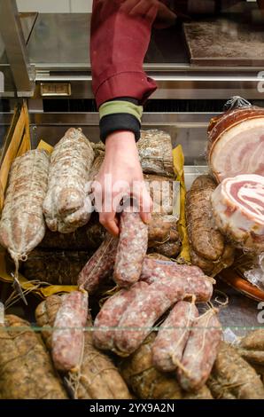 Cremona, Italien - 15. November 2020 Metzger, der an einem Marktstand in cremona, italien, gereifte Wurst aus verschiedenen Salami- und Fleischsorten auswählt Stockfoto