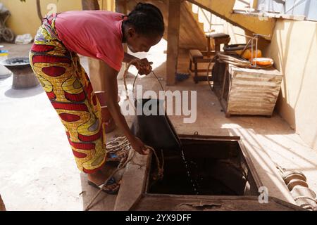 Junge afrikanische Mädchen, die Wasser aus einem unhygienischen Hausbrunnen sammeln; Konzept der fehlenden sauberen öffentlichen Wasserversorgung im ländlichen Westafrika Stockfoto