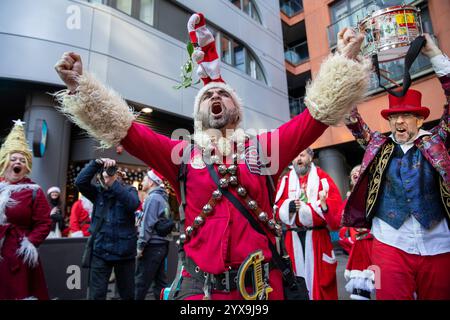 Ein Mann, der als Weihnachtsmann verkleidet ist, hebt die Arme. Hunderte von als Weihnachtsmann gekleideten Enthüllern nehmen an der Londoner Santa Con 2024 Teil. Mit seinen Anfängen in den Vereinigten Staaten ist Santa Con zu einem traditionellen Ereignis vor Weihnachten in London geworden. Die Santas-Parade beginnt zwei Wochen vor Weihnachten mit einem Kneipenbummel durch London, singen und schenken Zuschauern Geschenke. Während die überwiegende Mehrheit der Teilnehmer an Santa Con gutmütig und gut benommen ist, hat es in der Vergangenheit Trunkenheit und Gewalt gegeben. Stockfoto