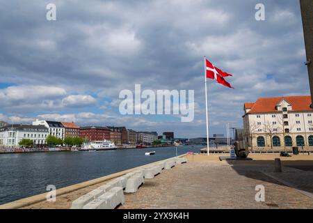 Eine winkende dänische Flagge am Ufer gegenüber dem berühmten Nyhavnon 29. April 2023 in Kopenhagen, Dänemark. Stockfoto