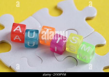 Wort Autismus gemacht mit bunten Würfeln und Puzzleteilen auf gelbem Hintergrund, Nahaufnahme Stockfoto