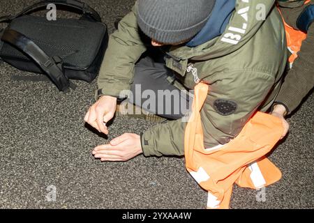 Ein Demonstrant mit einer orangefarbenen Weste wird während der Kundgebung auf die Straße geklebt. Aktivisten der Bewegung der letzten Generation und Mitglieder anderer Organisationen veranstalteten einen fünfstündigen Bürgerprotest in Warschau, um einen Ort des anhaltenden zivilen Widerstands zu schaffen. Die Demonstration begann um 17:00 Uhr. Auf der Gdanski-Brücke wurde ein großes Banner mit der Aufschrift „Apocalypse Now“ ausgestellt, das auf Chris Niedenthals ikonisches Foto vom 13. Dezember 1981 verweist. „Vor einundvierzig Jahren, während der Einführung des Kriegsrechts, fürchteten sich die Menschen um ihre Zukunft in Polen. Proteste wurden gewaltsam unterdrückt, und mA Stockfoto
