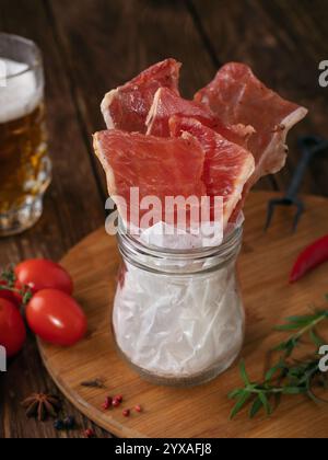 Rohe geräucherte Schweinefleisch-Chips für Bier im Glas auf Holztisch, Bier-Snack Stockfoto