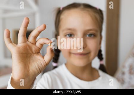 Das kleine kaukasische Mädchen lächelt, während es vor kurzem verlorenen Kinderzahn zu Hause hält, symbolisiert Meilenstein und Wachstum in der Kindheit. Stockfoto