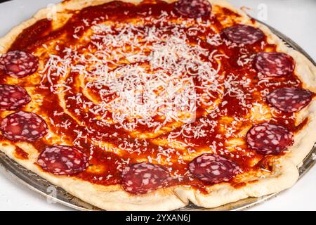 Pizza kochen, den Teig auf dem Backrad mit Tomatensoße einfetten, mit geriebenem Käse bestreuen und die Wurst bestreichen. Hochwertige Fotos Stockfoto