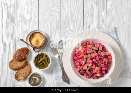 Rosolli, traditioneller finnischer weihnachtlicher Salat in weißer Schüssel auf weißem Holztisch mit Gabeln, Roggenbrot und hausgemachtem Dressing, horizontaler Blick Stockfoto