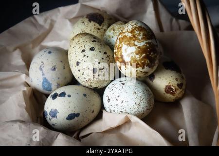 Eine Vielzahl gesprenkelter Eier in verschiedenen Farben und Mustern sind in einem rustikalen Korb mit Kraftpapier eingebettet und schaffen so eine ansprechende Präsentation. Stockfoto