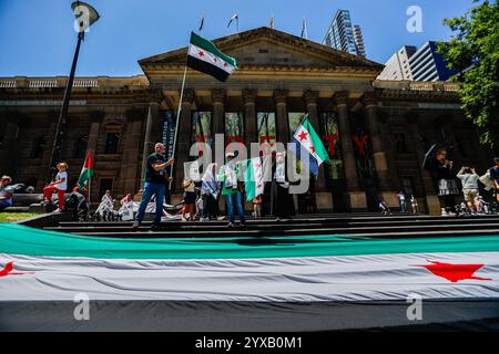 Melbourne, Australien. Dezember 2024. Die Demonstranten schwenken während der Kundgebung die Flagge Syriens. Die Demonstranten schwenken palästinensische Flaggen und halten Banner, die ein Ende des Völkermords und der zionistischen Aggression fordern, und rufen in Solidarität für die palästinensische Befreiung und Gerechtigkeit. (Foto: YE Myo Khant/SOPA Images/SIPA USA) Credit: SIPA USA/Alamy Live News Stockfoto