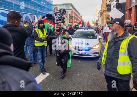 Birmingham, Großbritannien. DEZEMBER 2024. Demonstranten tanzt vor dem Polizeiauto, während eine pro Palestine Menschenmenge vom Handsworth Park ins Zentrum von Birmingham marschierte. Die Gruppe, einschließlich derer, die im Rahmen von Healthworkers 4 Palestine Peelings trugen, sang und zündete Fackeln an. Gruppen aus Liverpool und London schlossen sich an. Credit Milo Chandler/Alamy Live News Stockfoto