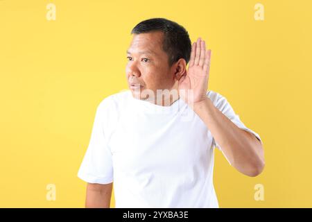 Asiatischer Mann im Mittelalter mit Hand auf dem Ohr, schlechte Nachrichten oder verlorenes Konzept. Isoliert auf gelbem Hintergrund Stockfoto