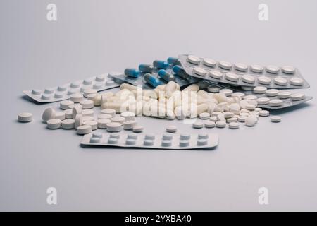 Verschiedene weiße Tabletten, blaue und weiße Kapseln und Blisterpackungen mit Tabletten sind auf einer weißen Oberfläche verstreut. Dieses Bild ist ideal zur Veranschaulichung Stockfoto