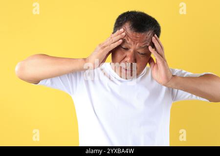 Emotionales Porträt eines Mannes mittleren Alters, der intensive Frustration und Wut zeigt, indem er seinen Kopf greift, isoliert auf gelbem Hintergrund. Stockfoto