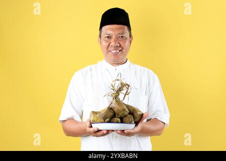 Asiatischer Mann im mittleren Alter mit Baju Koko, der Einen Teller Eof Ketupat-Reiskuchen für Lebaran IED Al Fitr hält Stockfoto