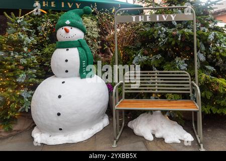 London, Großbritannien – 1. Dezember 2024, Covent Garden. Ein Schneemann mit grünem Hut und Schal steht vor Weihnachtsbäumen in der Nähe des Restaurants „The Ivy“ Stockfoto