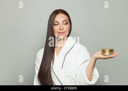 Fröhliche brünette Frau, die eine Creme Tube Box in ihrer Handhand auf weißem Hintergrund zeigt Stockfoto