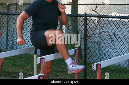 Ein Mann führt Hürdenübungen in einem Sportbereich im Freien durch, wobei er sich auf Agilität und Geschwindigkeitstraining konzentriert. Stockfoto