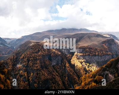 Herbstlich getrocknete braune Bäume auf vielen komplexen Felshügeln und Bergen auf weißen Wolken und blauem Himmel Hintergrund, Blick auf Georgia Country. Wunderschöner Berg Stockfoto