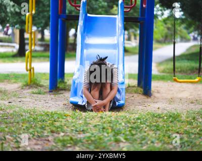 Ein trauriges kleines Mädchen sitzt allein auf einer Spielplatzrutsche. Ein unglückliches Kind spielt allein. Stockfoto