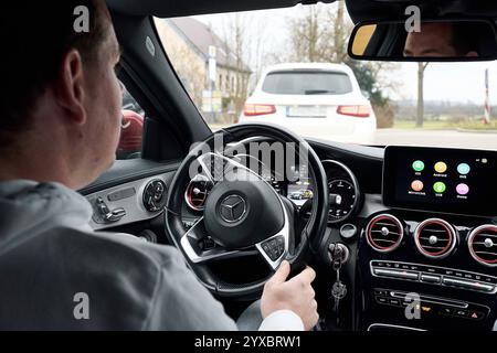 Bayern, Deutschland - 14. Dezember 2024: Ein junger Mann sitzt am Lenkrad eines Autos, während er auf einer Straße fährt. Der Innenraum zeigt ein modernes Armaturenbrett mit integriertem Display und Multimedia-Funktionen sowie CarPlay und Android Auto *** ein junger Mann sitzt am Steuer eines Autos, während er auf einer Straße fährt. Der Innenraum zeigt ein modernes Dashboard mit integriertem Display und Multimedia-Funktionen sowie CarPlay und Android Auto Stockfoto