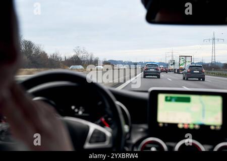 Bayern, Deutschland - 14. Dezember 2024: Ein junger Mann fährt mit dem Auto auf der Autobahn. Auf dem Bildschirm des Navigationssystems wird Google Maps angezeigt, das eine Route *** ein junger Mann fährt ein Auto auf der Autobahn anzeigt. Auf dem Bildschirm des Navigationssystems ist Google Maps zu sehen, das eine Route angezeigt Stockfoto