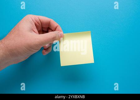 Hand mit leerem gelbem Post-it auf blauem Hintergrund Stockfoto