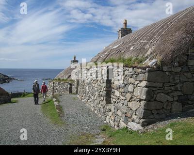 Touristen-Paar in traditionellen alten, strohgedeckten alten, schwarzen Häusern im Gearrannan Blackhouse Village, Isle of Lewis, Äußere Hebriden, Schottland, Großbritannien Stockfoto