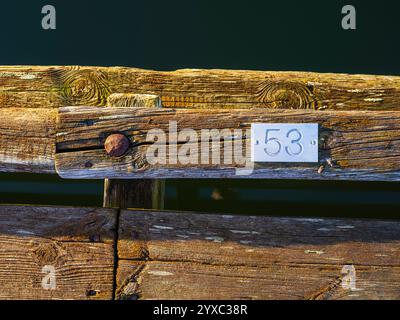 Ein verwitterter hölzerner Pier erstreckt sich über das ruhige Wasser, mit einem Nummernschild, das 53 an der Seite zeigt und von warmem Sonnenuntergang beleuchtet wird. Stockfoto