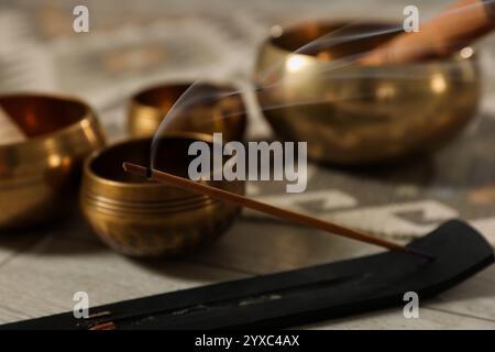 Räucherstäbchen schwelend im Halter und tibetische Klangschalen auf dem Boden, Nahaufnahme Stockfoto