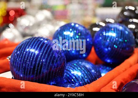 Weihnachtsspielzeug, blaue Kugeln im roten Korb auf verschwommenem festlichem Lichthintergrund. Neujahrsdekoration in einem Laden Stockfoto