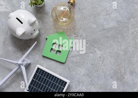 Windturbine mit Solarmodul, Hausfigur, Glühbirne und Schweinebank auf Grunge-Hintergrund. Konzept der grünen Energie Stockfoto