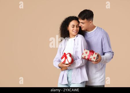 Liebevolles junges Paar, das Geschenkboxen auf beigefarbenem Hintergrund austauscht. Valentinstag-Feier Stockfoto