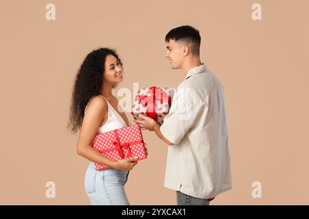 Liebevolles junges Paar, das Geschenkboxen auf beigefarbenem Hintergrund austauscht. Valentinstag-Feier Stockfoto