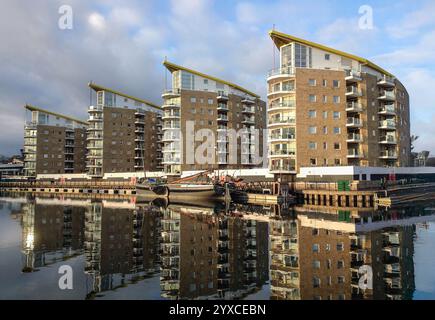 Moderne Wohnblocks mit alten Booten, die auf dem River Lee liegen, spiegeln sich in Water, London, England, Großbritannien Stockfoto