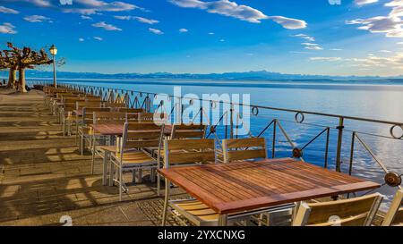 Promenade in Meersburg mit spannendem Blick auf den Bodensee, die Schweiz und die Alpen an einem sonnigen Wintertag. Leere Tische auf dem Stuhl am Ufer von Stockfoto