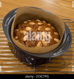 Kleiner, runder, frisch gebackener Dundee Cake mit Mandeln, noch in gefütterter Backform auf Kühlregal. Stockfoto