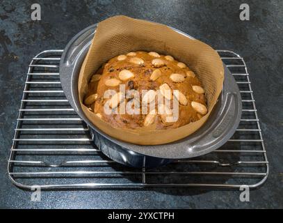 Kleiner, runder, frisch gebackener Dundee Cake mit Mandeln, noch in gefütterter Backform auf Kühlregal. Stockfoto