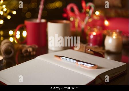 Eine einladende Winterszene mit einer beleuchteten Kerze, Tassen, Zuckerstangen und einem Notizbuch mit Stift. Stockfoto