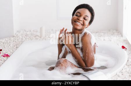 Frau mit geschlossenen Augen des Vergnügens Baden mit Schaum Und Blütenblätter zu Hause Stockfoto
