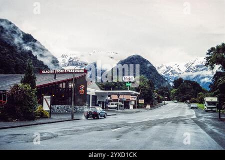 Franz Josef / Waiau, Westküste Neuseelands Südinsel. Archivfoto der Hauptstraße (State Highway 6) der kleinen Stadt aus dem Jahr 1991 mit Bergen im Hintergrund Stockfoto