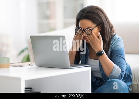 Frau, die tagsüber Frustration empfindet, während sie zu Hause an einem Laptop arbeitet Stockfoto
