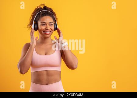 Frau genießt Musik, während sie Kopfhörer auf einem hellgelben Hintergrund trägt Stockfoto