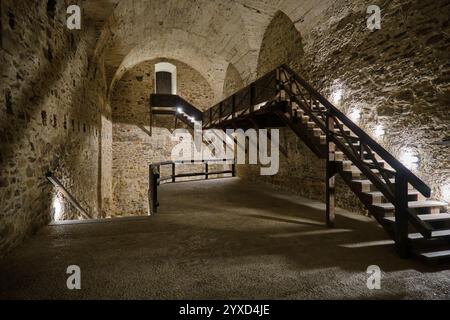 Eine Holztreppe erhebt sich entlang einer Mauer in den großen Kellern des Roten Steinschlosses in der Slowakei. Stockfoto